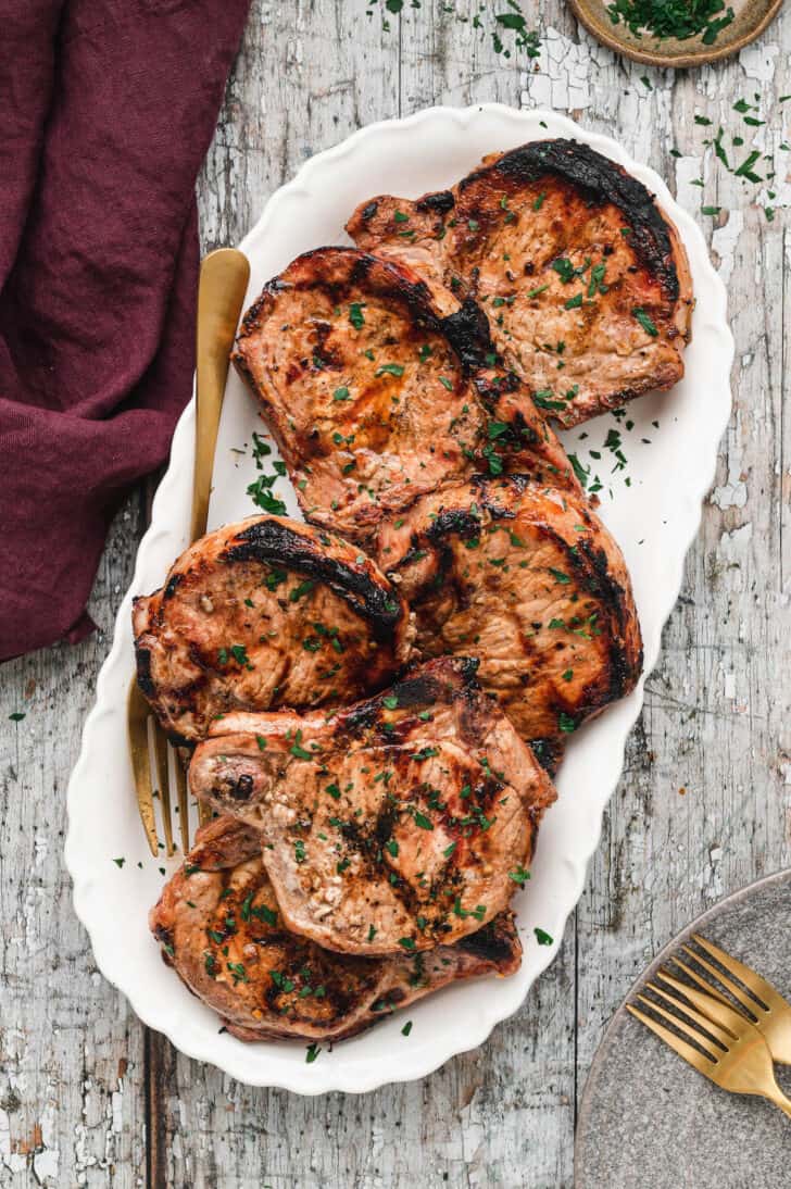 An oblong white platter topped with grilled pork chop, on a rustic surface.