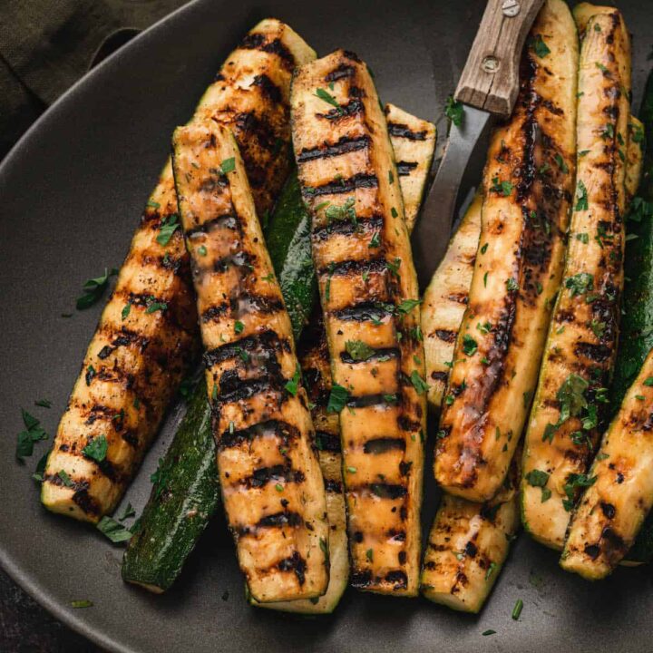Grilled zucchini spears with a miso glaze on a dark gray oval platter.