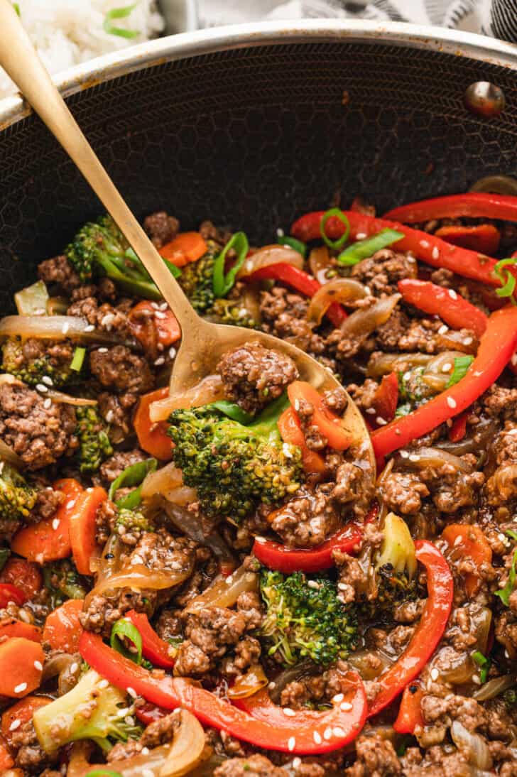 Gold spoon lifting up some stir fry ground beef and vegetables mixture.