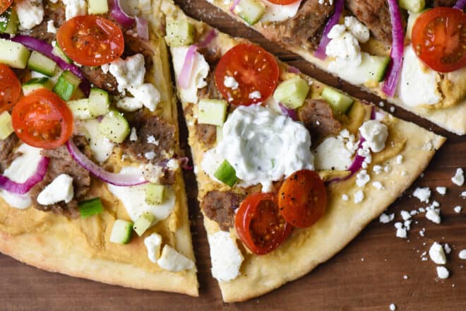 Closeup on flatbread topped with lamb meat, tomatoes, red onion, cucumber and tzatziki sauce.