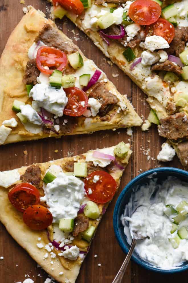 Closeup on two slices of mediterranean flatbread on wooden surface with small blue bowl of yogurt sauce.