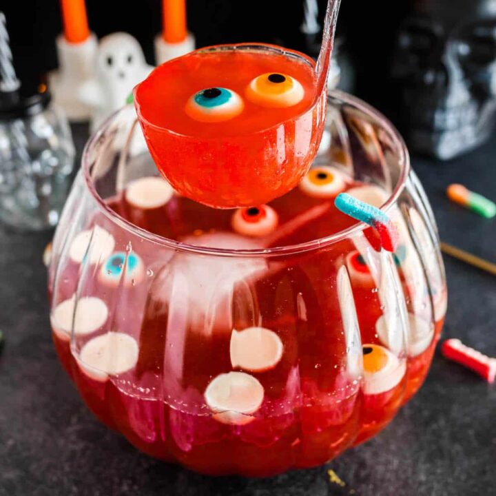 A glass bowl filled with red Halloween punch and gummy eyeballs, with a ladle lifting a serving out.