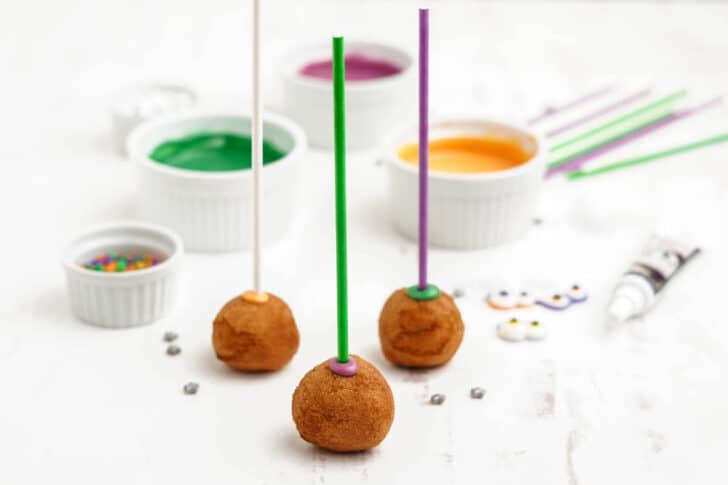 Donut holes skewered with colored lollipop sticks, on a light surface.
