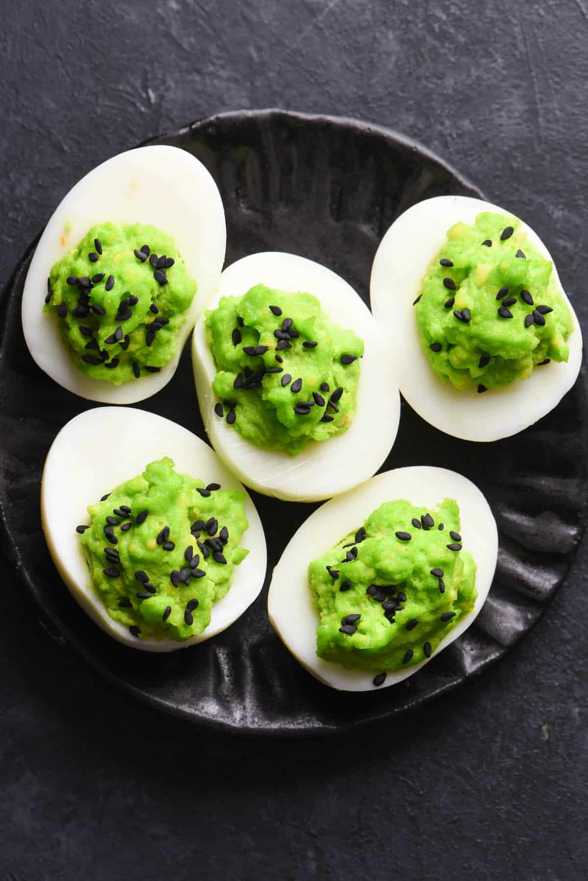 Spooky deviled eggs with dyed neon green yolks, decorated with black sesame seeds.