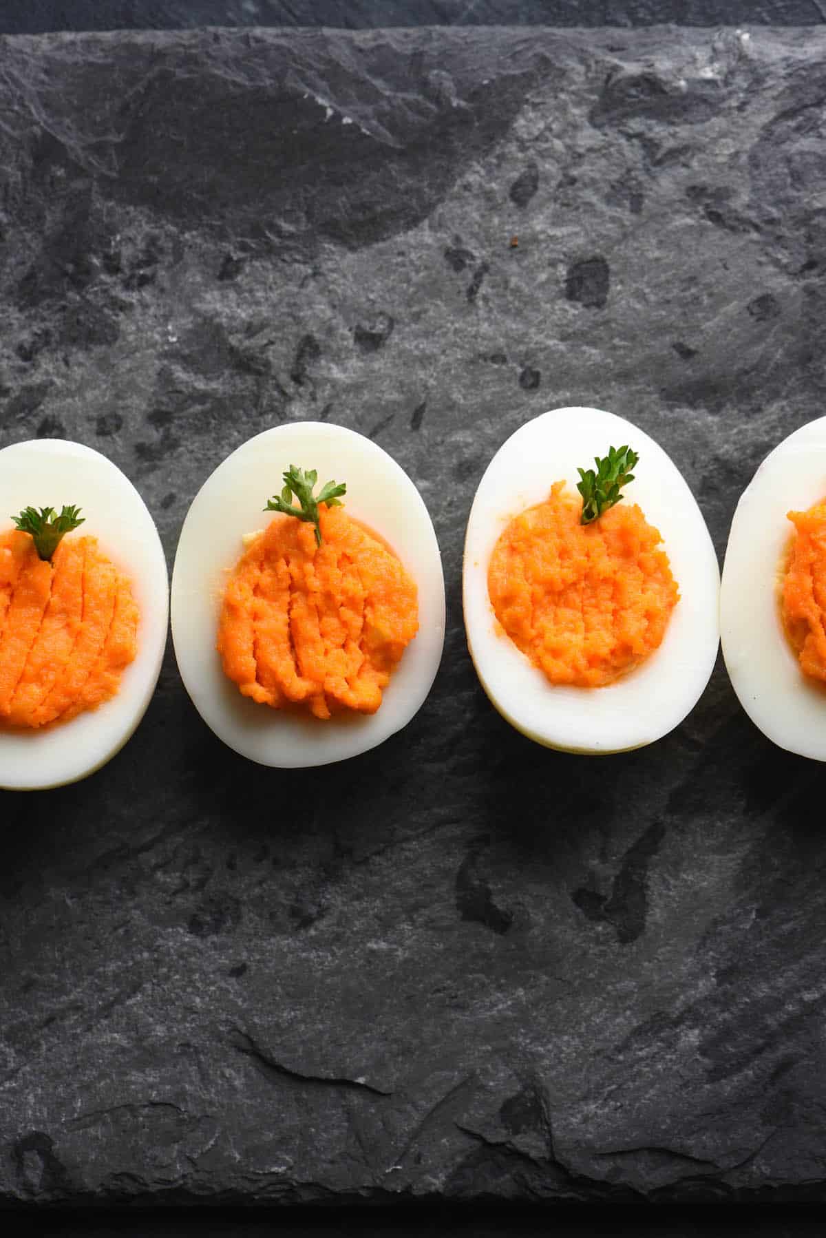 Pumpkin deviled eggs with orange yolks, decorated with parsley "stems."