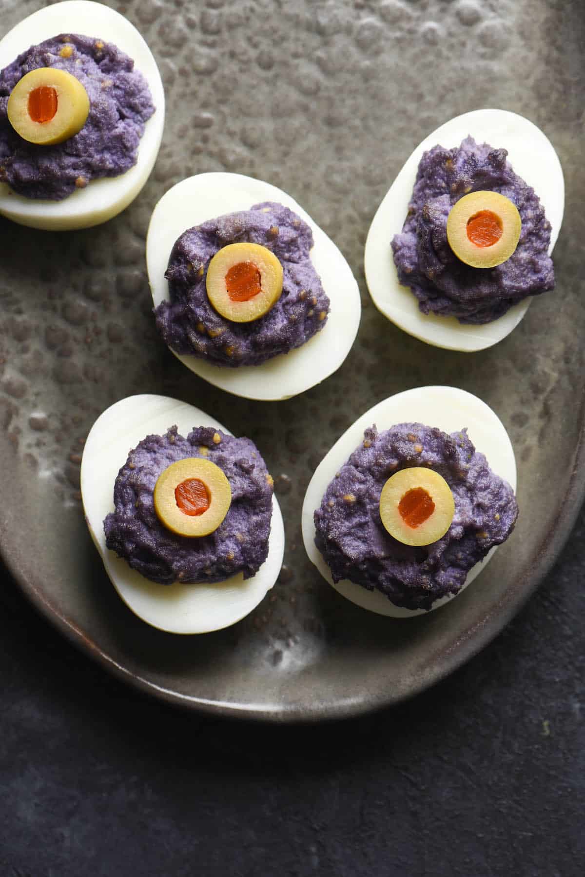 Eyeball deviled eggs with dyed purple yolks and green olive "eyeballs" on top.