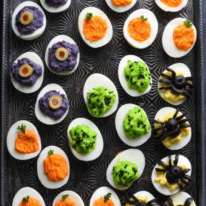 Cookie sheet with various types of Halloween deviled eggs arranged on top.