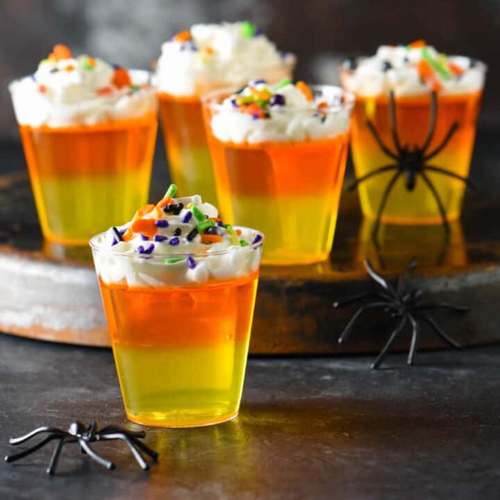 Halloween Jello shots made with layers of yellow and orange Jello and whipped cream, topped with sprinkles.