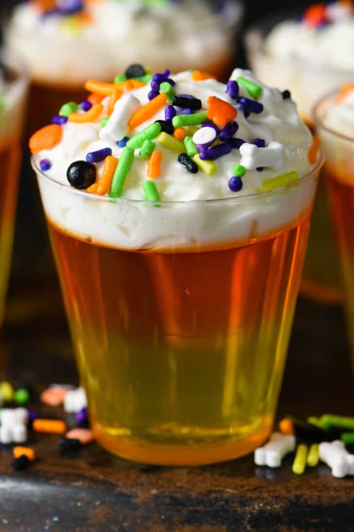 A layered yellow, orange and white Halloween Jello shot topped with festive sprinkles.