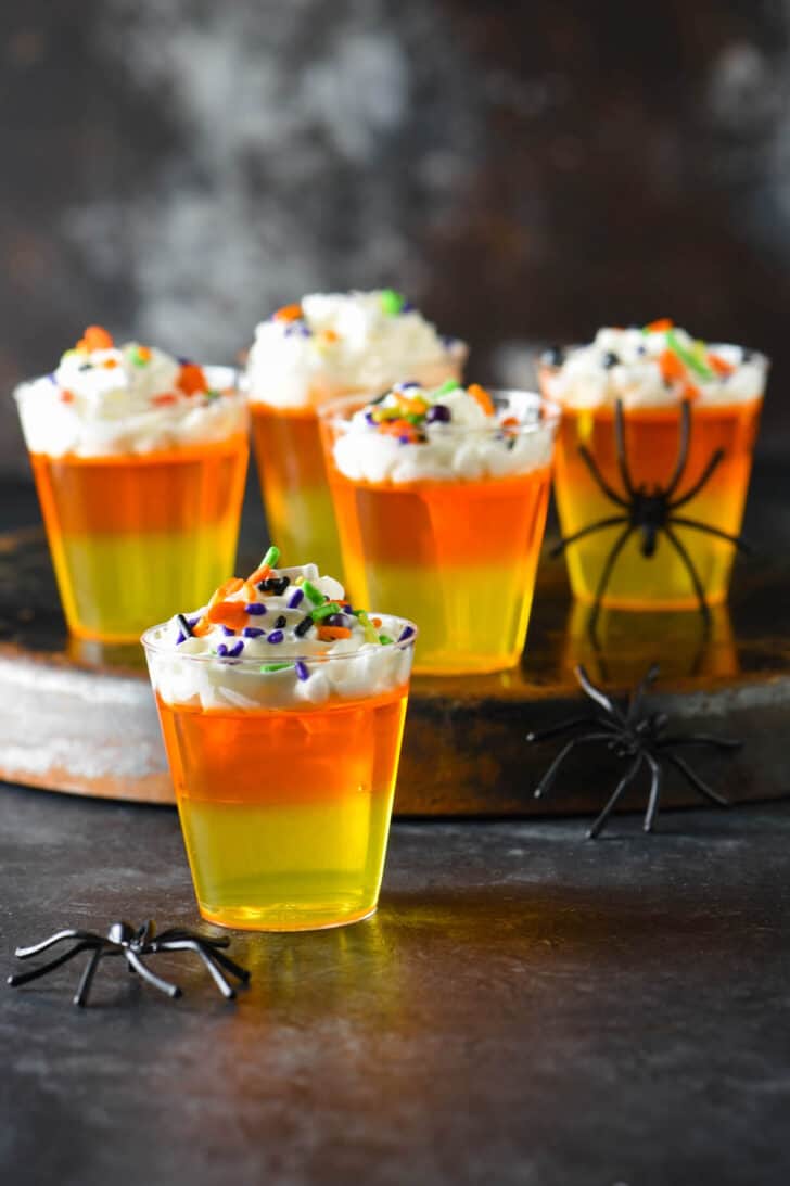 Halloween Jello shots made with layers of yellow and orange Jello and whipped cream, topped with sprinkles.