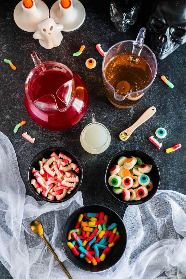 Ingredients needed for a spooky beverage, including red juice, ginger ale, coconut water and gummy candies.