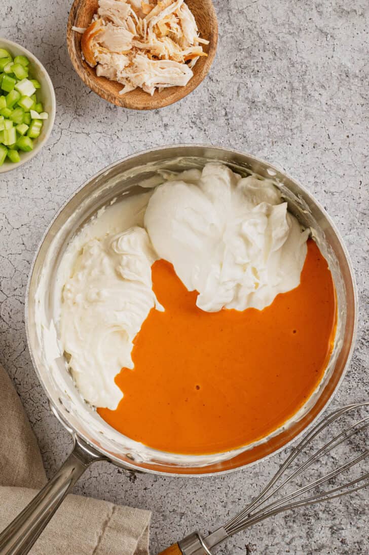 The ingredients for healthier buffalo chicken dip in a saucepan, including buffalo sauce, Greek yogurt and lowfat cream cheese.