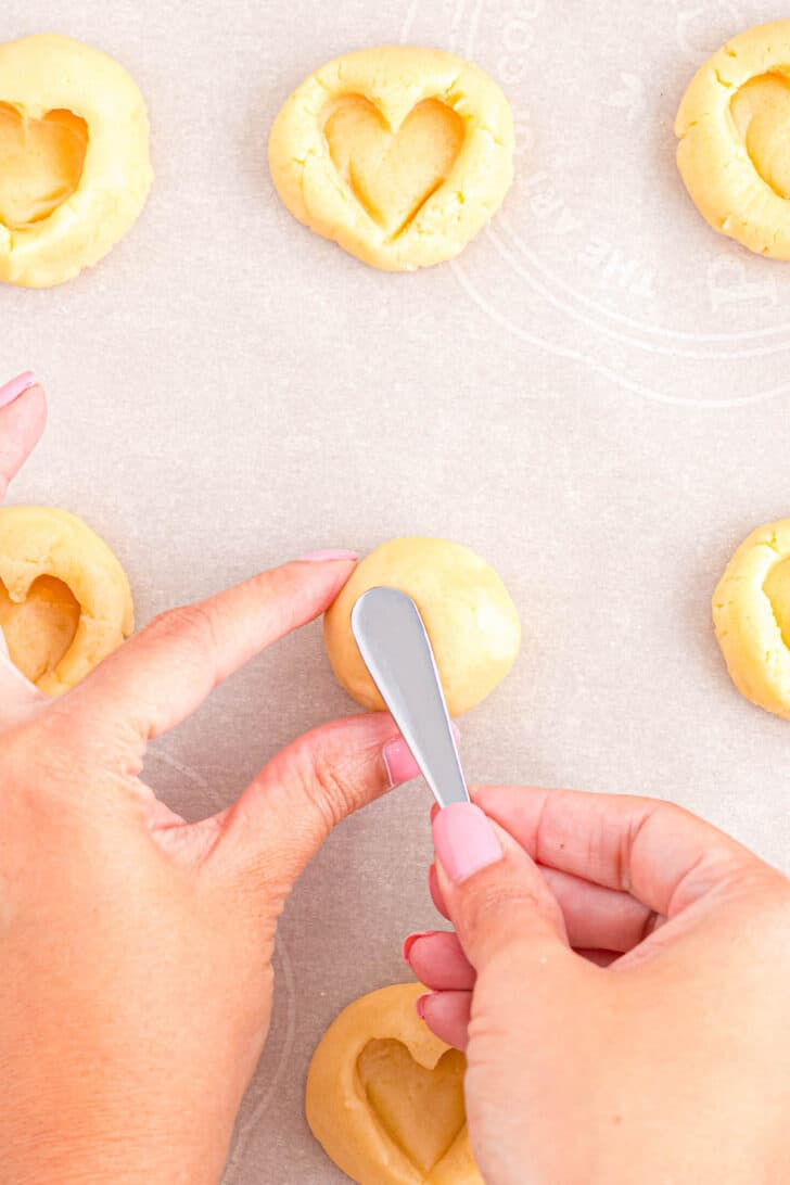 Hands using an espresso spoon to stamp shortbread cookies into heart cookies.