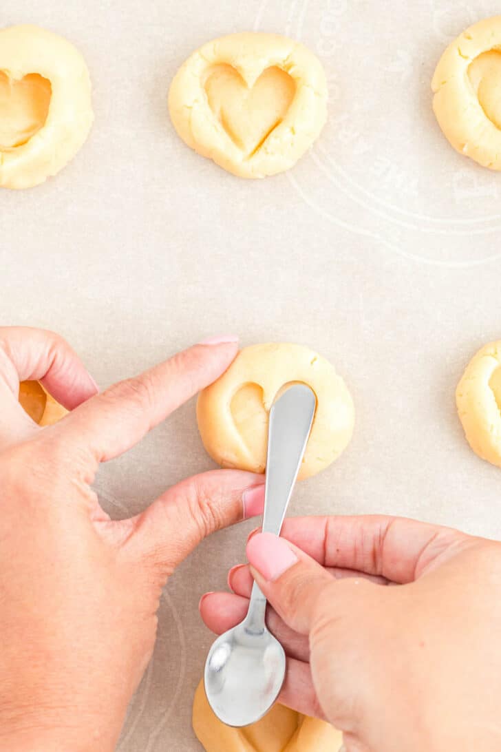 Hands making shortbread thumbprint cookies with a small spoon.