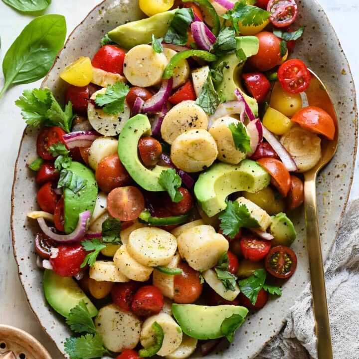 A speckled oval platter filled with hearts of palm salad made with tomatoes and avocado.