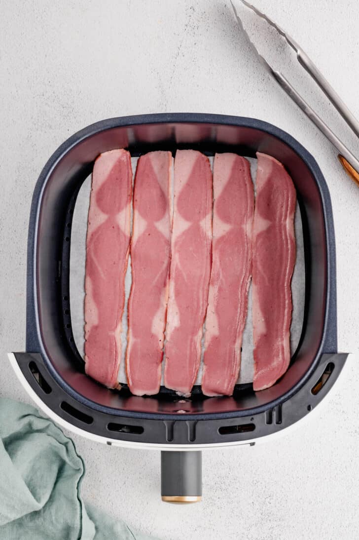 Five raw slices of turkey bacon in an air fryer basket.