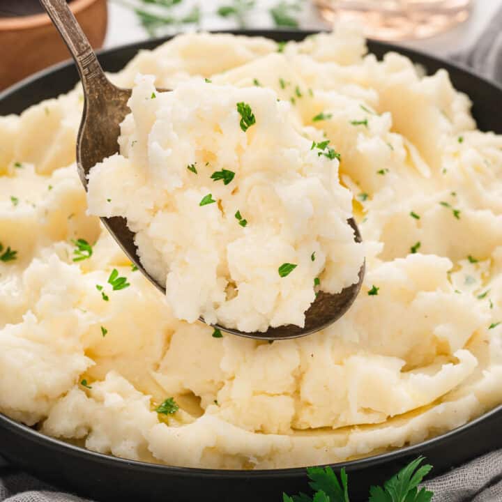 A bowl of a creamy mashed potatoes recipe with a spoon lifting some up.