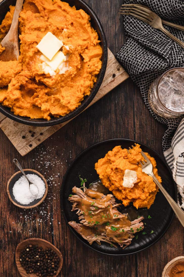 A black plate filled with pulled meat and mashed sweet potatoes topped with butter.