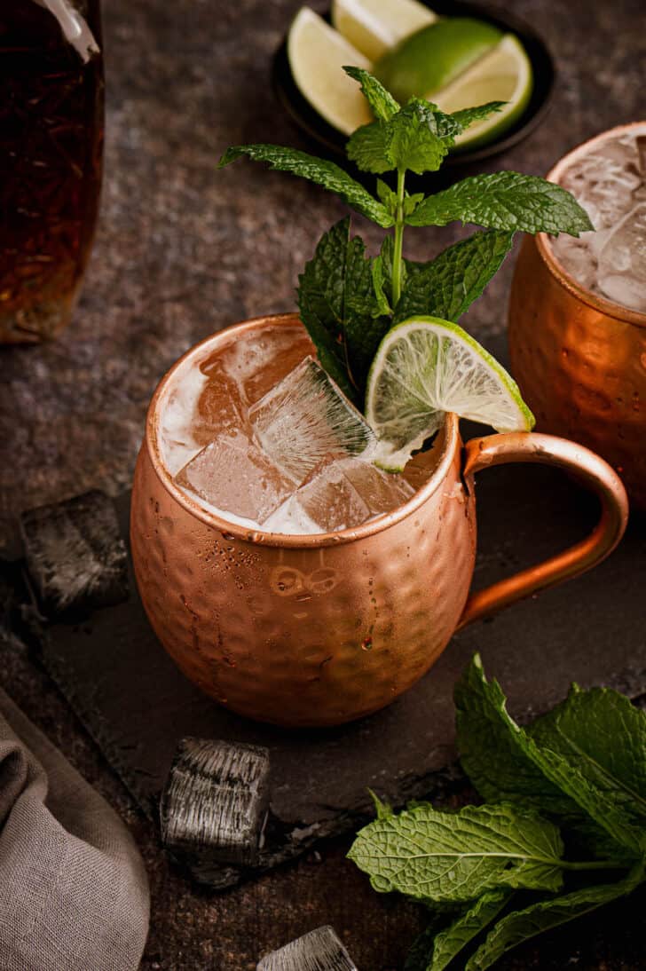 A hammered copper mug filled with ice cubes and clear liquid, garnished with limes and mint.
