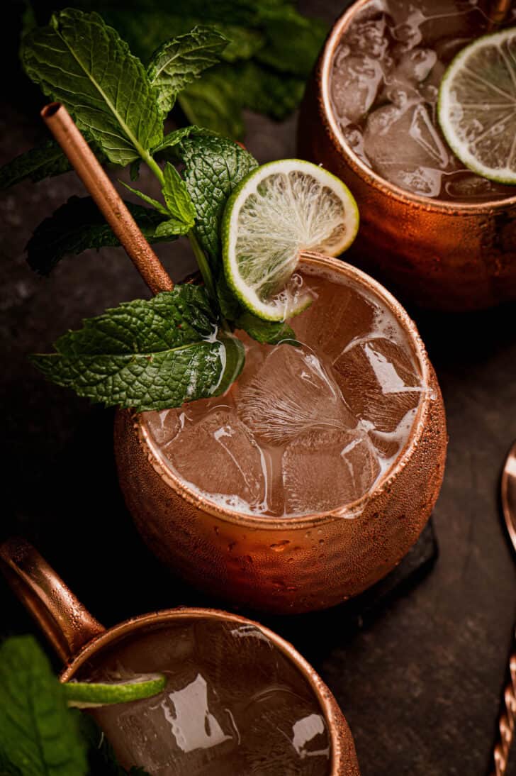 Overhead image of bourbon mule cocktails in copper mugs with lots of ice, garnished with mint leaves and lime wheels.