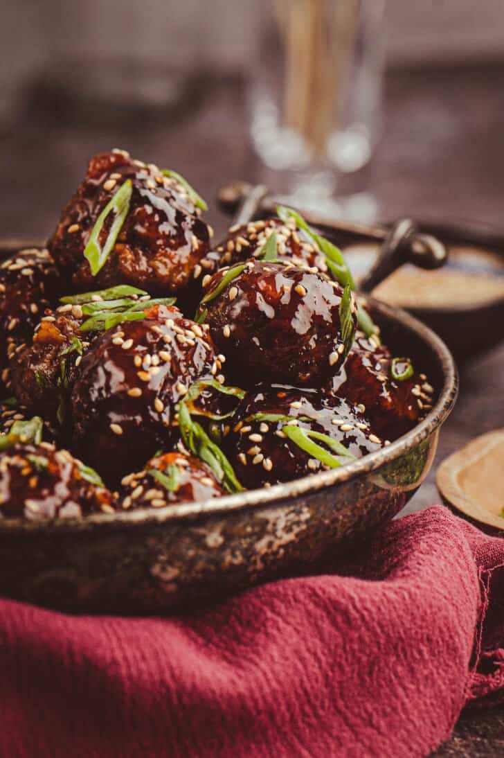 Korean style meatballs piled high in a metal bowl, garnished with green onions and sesame seeds.