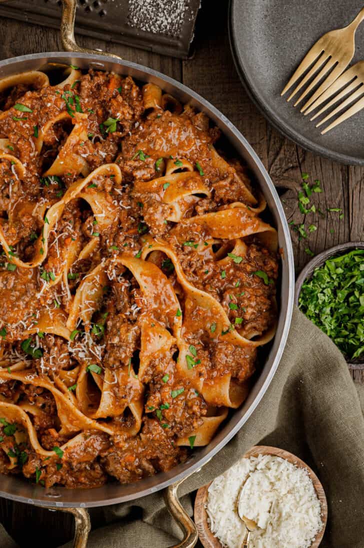 A large skillet filled with lamb pasta made with pappardelle noodles, garnished with parsley.
