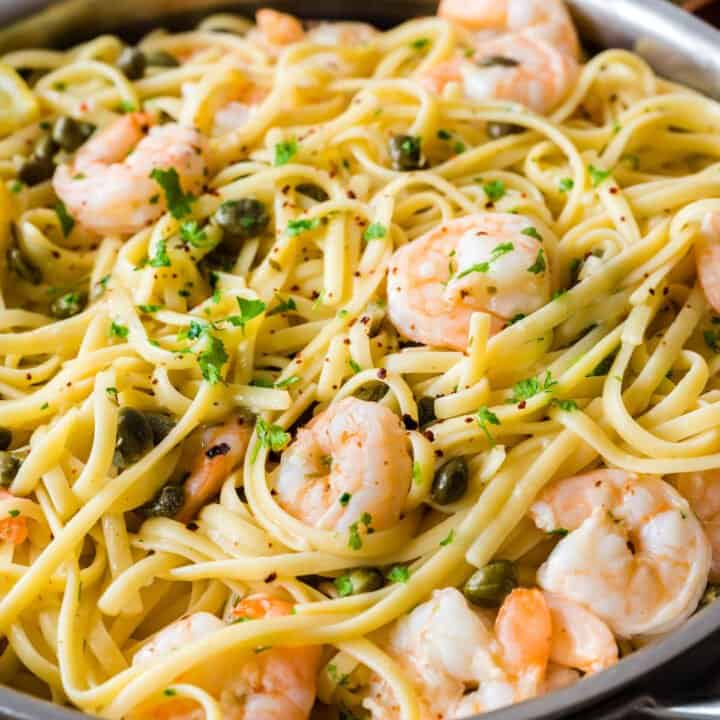 Stainless steel skillet filled with linguine and shrimp dressed with a caper and herb sauce.
