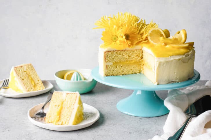 Cake slices filled with lemon curd and decorated with lemon curd buttercream on small plates, with the rest of the cake on a teal cake stand.