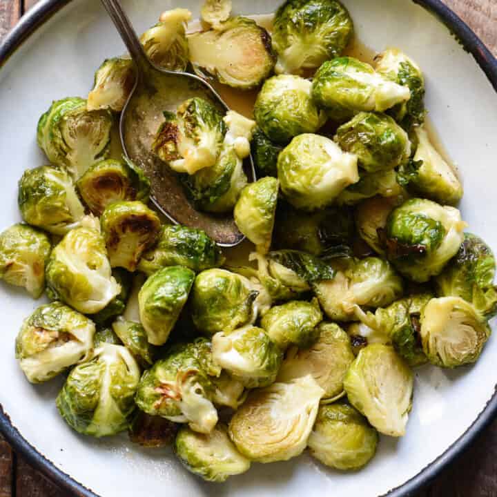 Rustic white bowl with blue rim, filled with maple glazed Brussels sprouts.