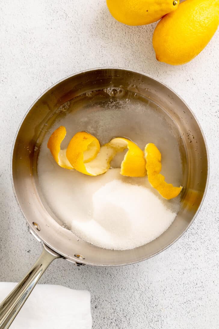 A small saucepan filled with water, sugar and spirals of lemon peel.