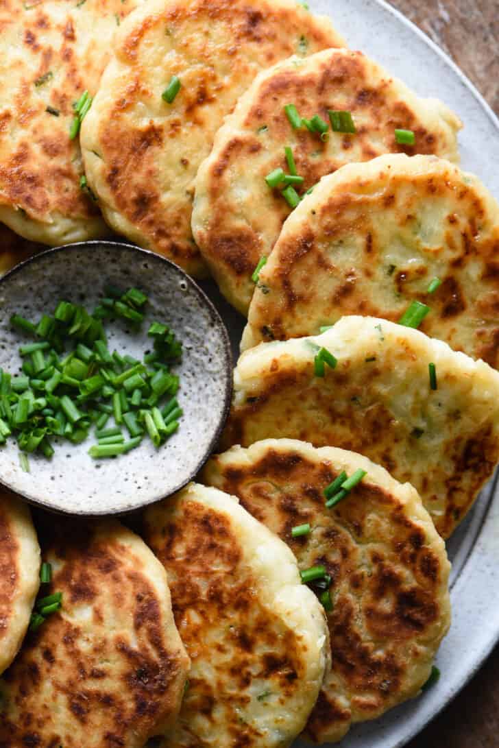 Mashed potato cakes arranged in a semi circle near a small bowl of sliced chives.