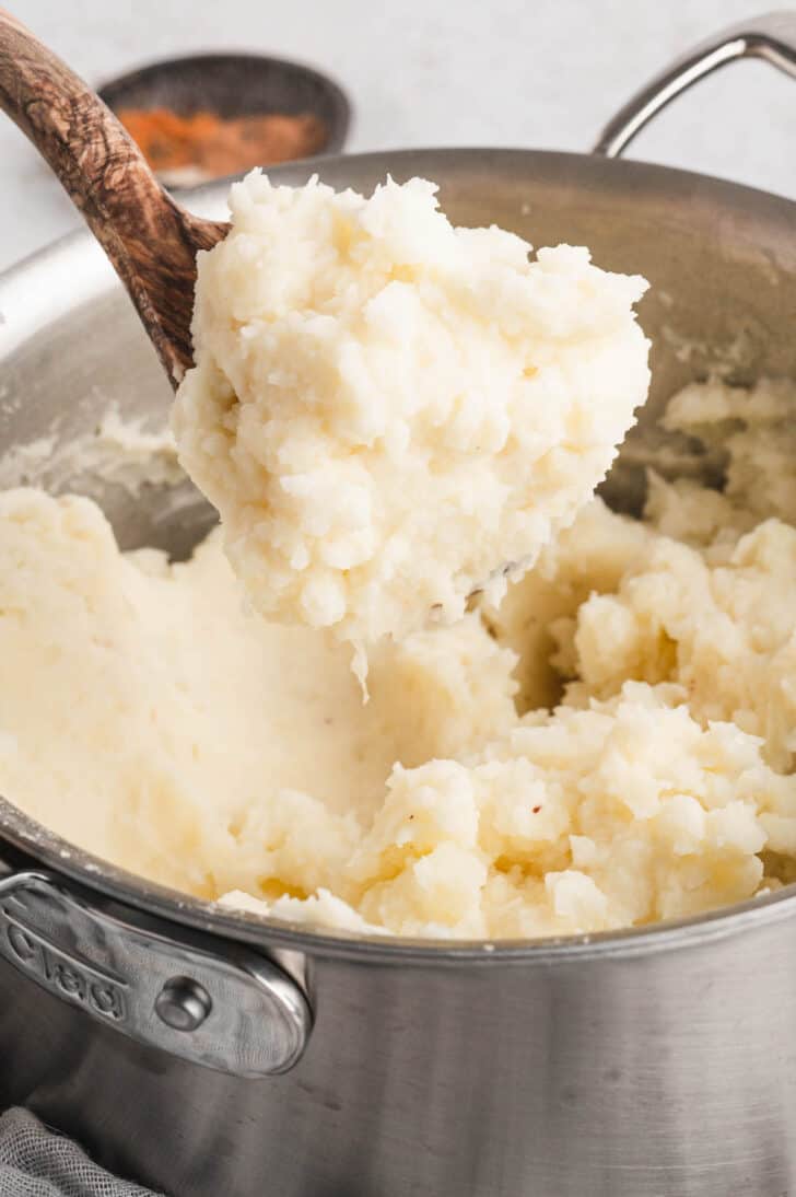 Mashed potatoes with heavy cream being lifted out of a pot with a wooden spoon.