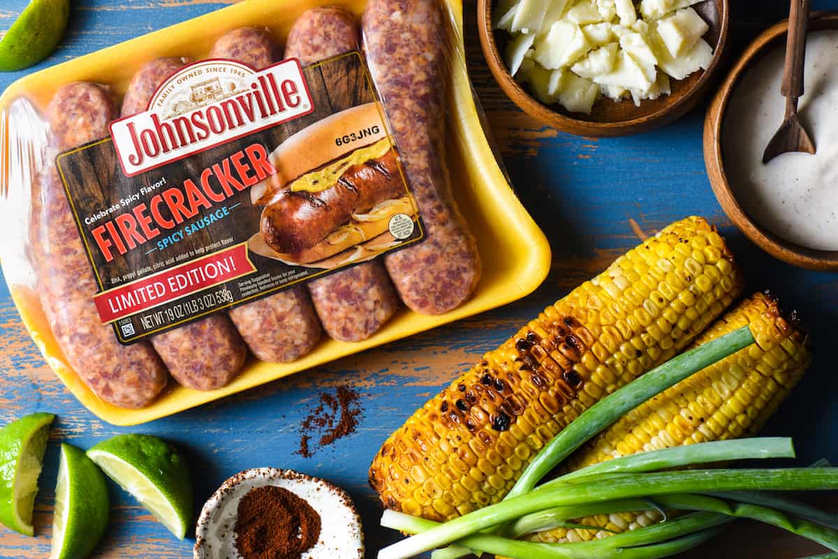 Inspired by elote, these Mexican Street Corn Brats are ideal for a summer celebration or easy weeknight meal! Spicy sausages are topped with fresh sweet corn, creamy lime sauce and tangy cheese. | foxeslovelemons.com