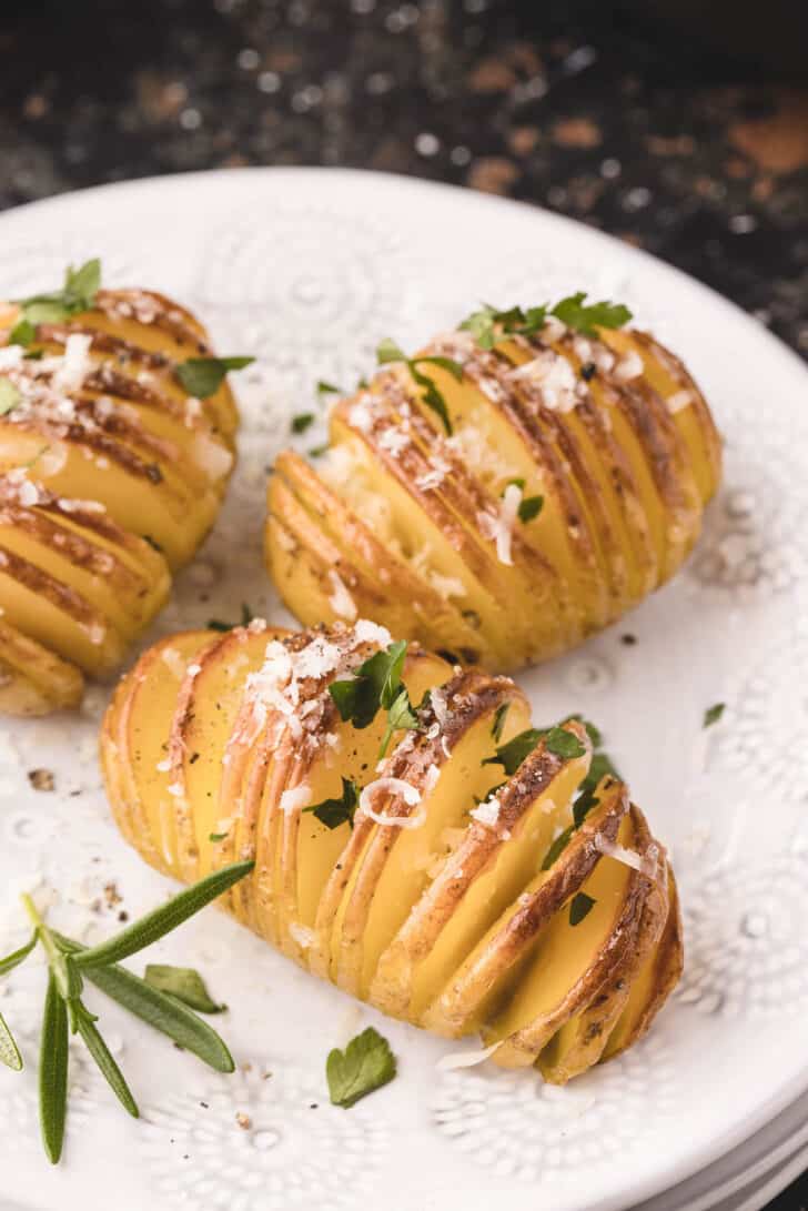 Potatoes cut in an according cut, sprinkled with herbs and cheese, on a textured white plate.
