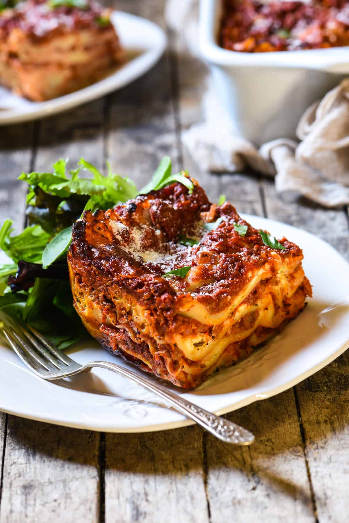 Piece of lasagna recipe with cottage cheese with a side salad on a rustic white plate.
