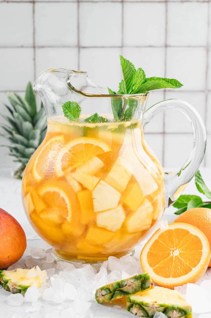 A large glass pitcher full of pineapple sangria, garnished with mint sprigs.