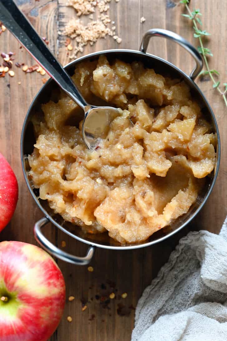 A metal bowl filled with mashed cooked apples, with a spoon in it.