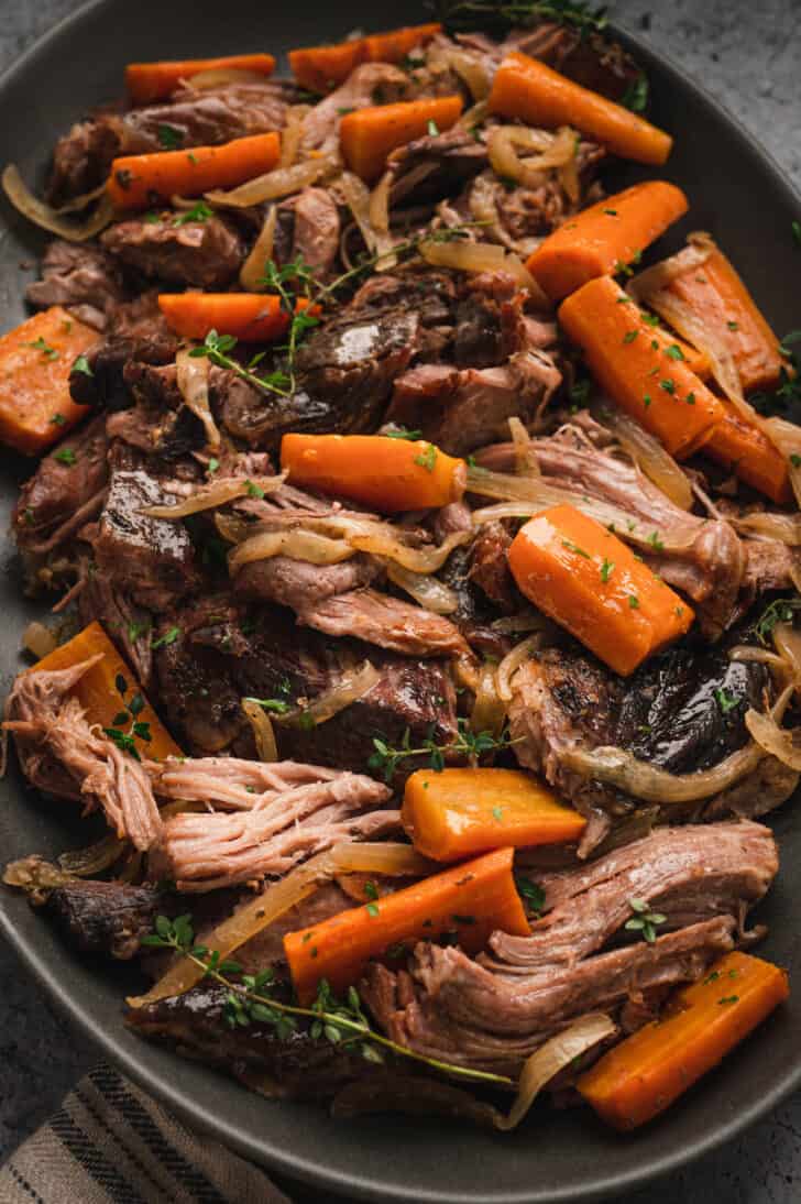 A platter of pork roast crock pot with onions, thyme and carrots.