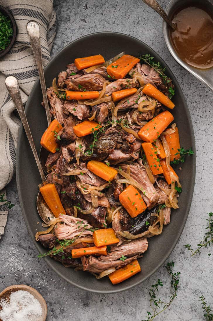 A platter of pork roast in slow cooker with onions, thyme and carrots.