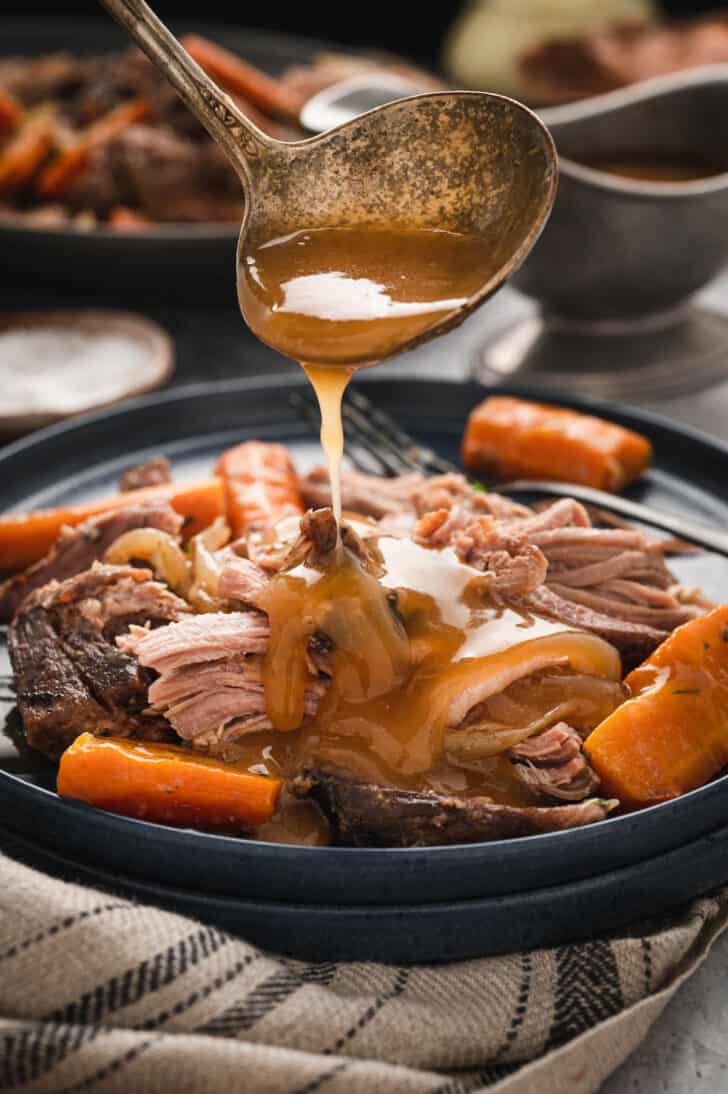 A plate of crockpot pork roast with onions, thyme and carrots, and gravy being drizzled over it.