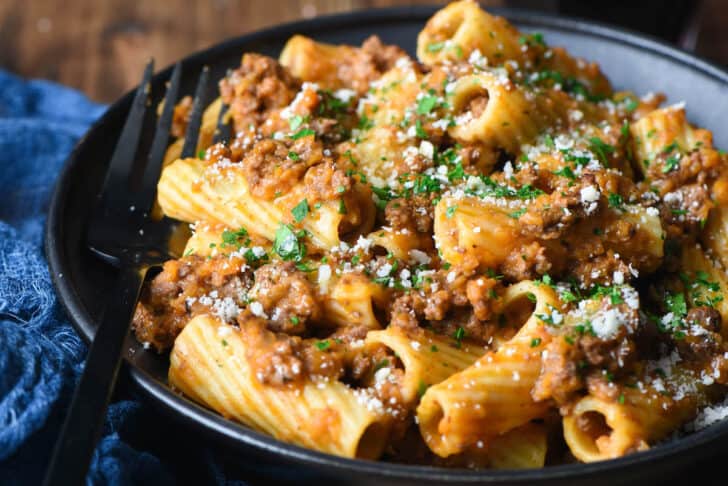 Black bowl filled with pasta and meat sauce, with black fork digging in.