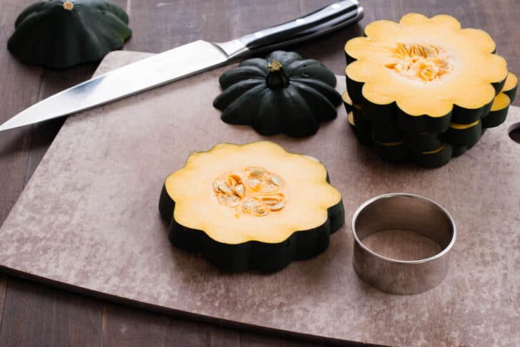Fall gourd cut crosswise into slices, on a brown cutting board with a chef's knife and a ring mold.
