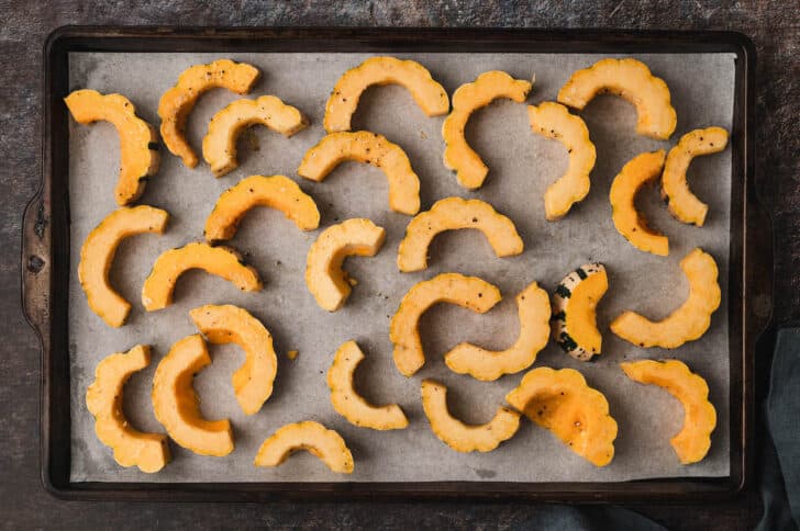 A baking pan topped with half moon slices of a fall gourd.