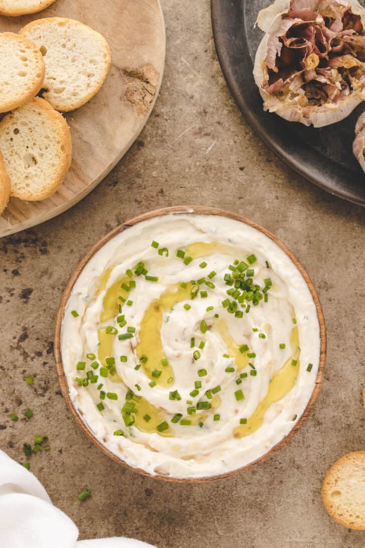 A round bowl filled with a creamy mixture garnished with chives and oil.