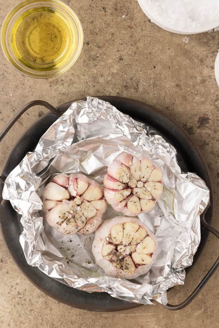 Raw heads of garlic with their tops cut off, in a foil packet, sprinkled with salt and pepper.