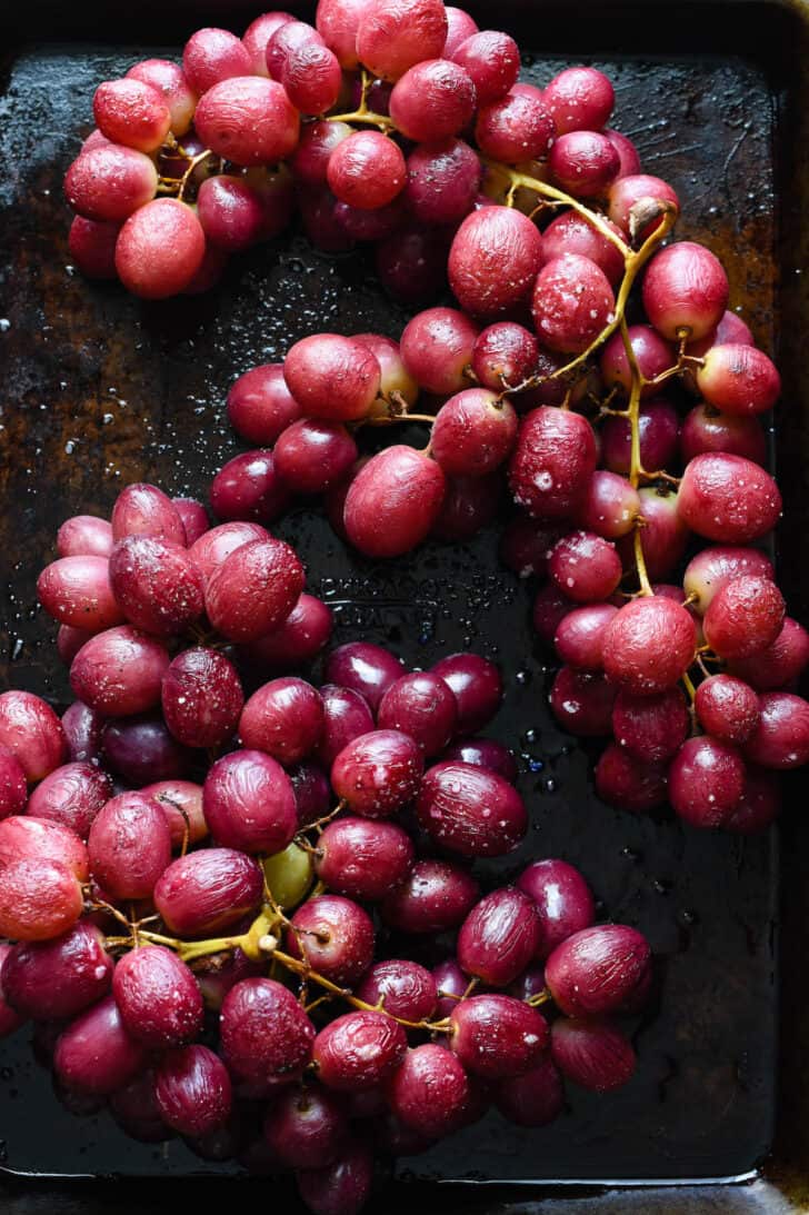 Red roasted grapes on their vines on a small dark baking pan.