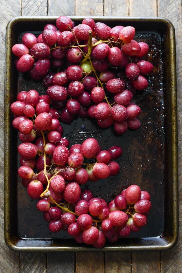 Roasted red grapes on their vines on a small dark baking pan.