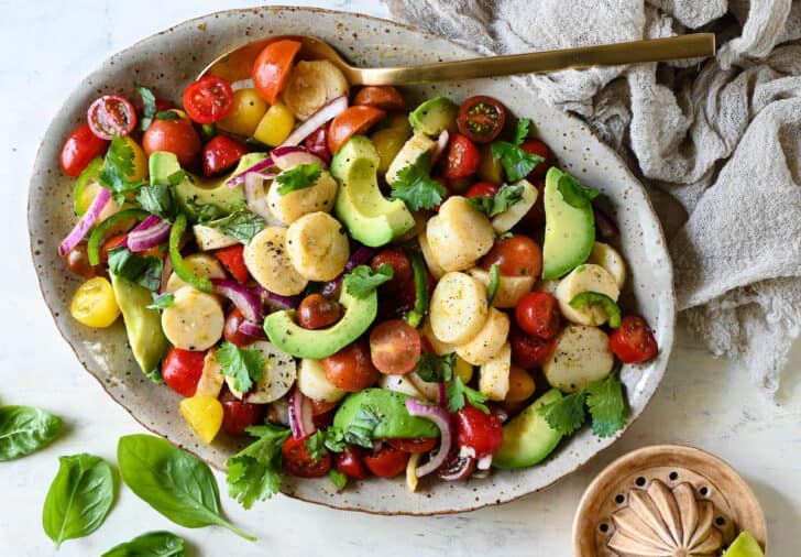 A speckled oval platter filled with palmito and avocado salad made with tomatoes and herbs.
