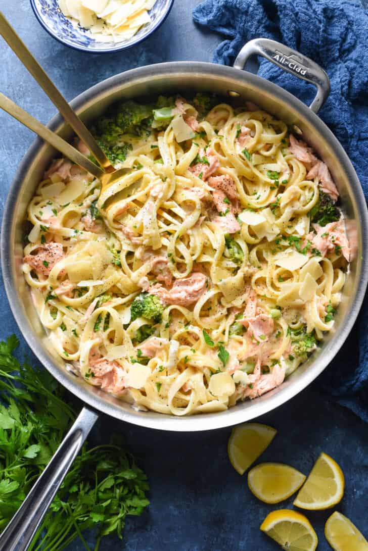 A large stainless steel skillet filled with salmon alfredo pasta and broccoli.