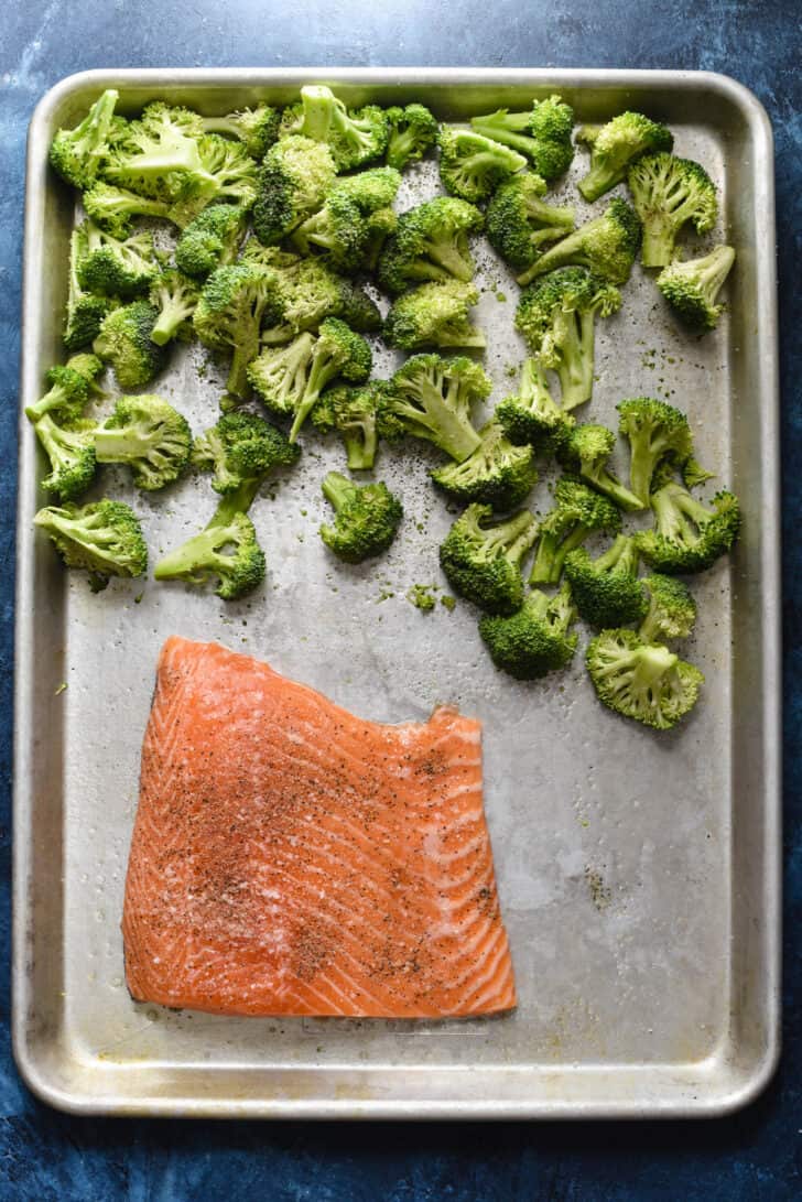 A stainless steel baking pan with cut up broccoli and a fillet of pink fish on it.
